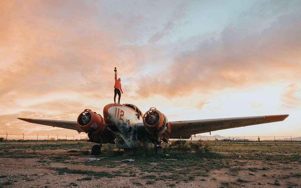 chico subido encima de una avioneta con la puesta de sol detrás